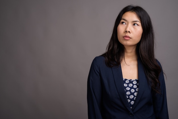 Asian woman wearing blue dress and cardigan sweater against gray space