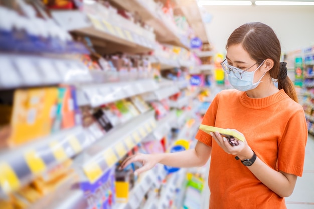 Asian woman wearing face mask for healthy walking at shopping mart choice products at supermarket shelf.