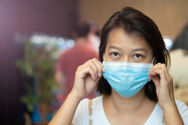 Asian woman wearing protective mask on her face while being in the coffee shop during virus COVID-19 pandemic.