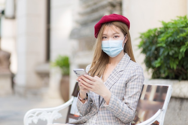 Asian woman wearing suit holds smartphone wearing medical face mask in new normal  concept