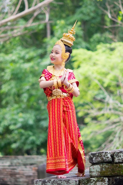 Asian woman wearing typical traditional Thai Dress standing on an antique stone ladder