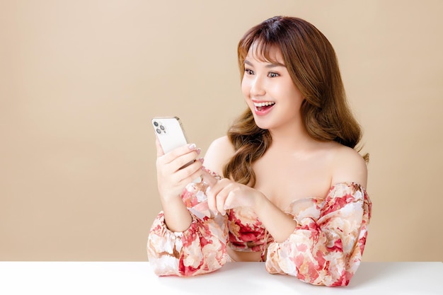 Asian woman with a beautiful face and Perfect clean fresh skin Portrait of female model Holding and looking at mobile phone on beige isolated background Cosmetology Body care plastic surgery