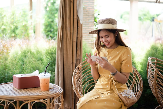 Asian woman with beautiful smile reading good news on mobile phone during rest in coffee shop happy female watching her photos on cell phone while relaxing in cafe during free time