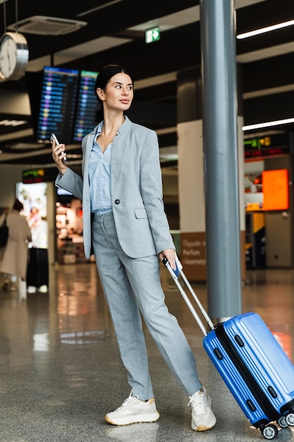 Photo asian woman with blue suitcase walks to the escalator in the airport terminal journey and vacation concept travel blogger is waiting for a new trip in the summer season of 2024