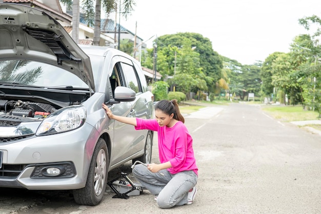 Asian woman with a car jack and wrench changing the car wheels