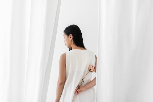 Asian woman with a dry pink peony flower in a hand among the white curtain