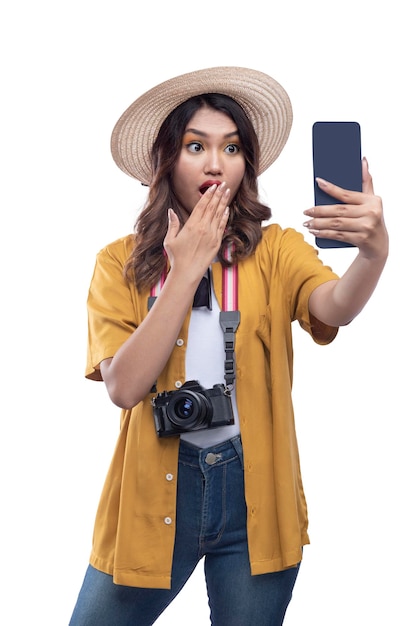 Asian woman with a hat and camera holding mobile phone with shocked expression