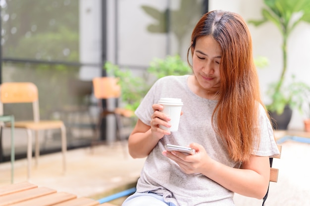 Asian woman with mobile phone and drinking coffee alone . Relax and recreation at botanic garden on holiday.