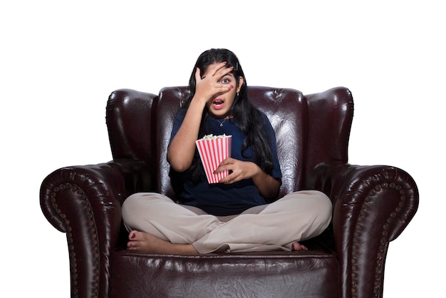 Asian woman with popcorn sitting on the couch with a scared expression