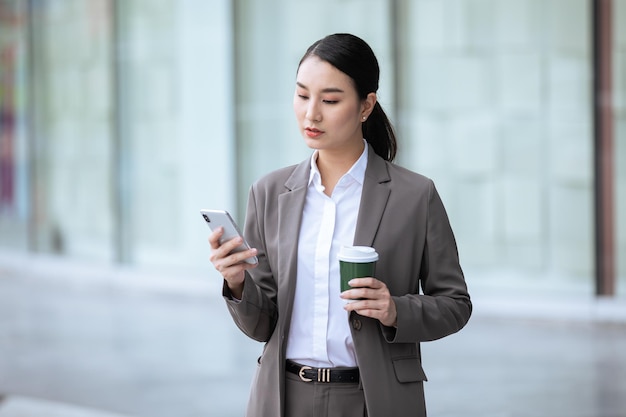 Asian woman with smartphone standing against street blurred building background Fashion business ph