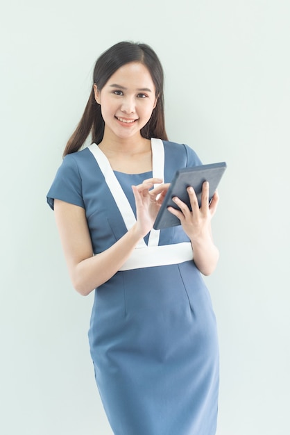 Asian woman with a tablet computer. Asian business woman using digital tablet computer, leaning against a grey wall.