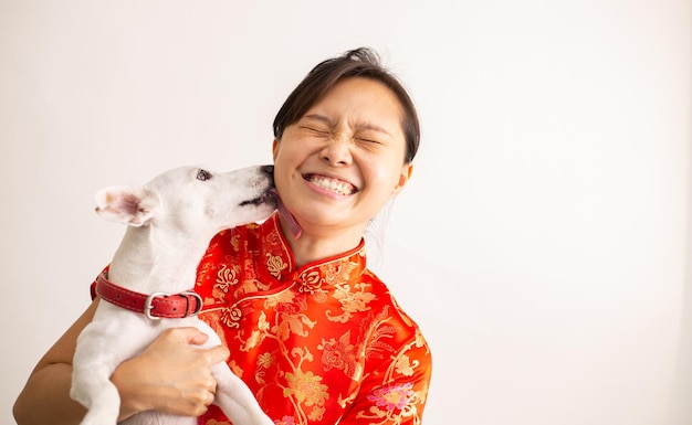 Asian woman with traditional red Chinese dress and jack russell terrier. A dog licking owner face for show love.Cute friendship.