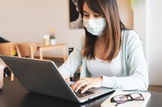 asian woman working on computer while wearing medical mask in cafe during the coronavirus crisis