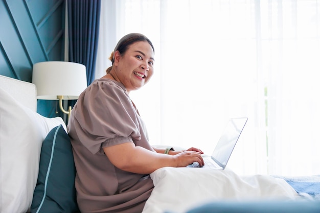 Asian woman working on laptop at home on the bed through internet for her business