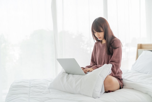 Asian woman working with laptop on bed at home