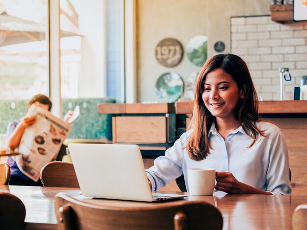 Asian woman working with laptop in coffee shop.