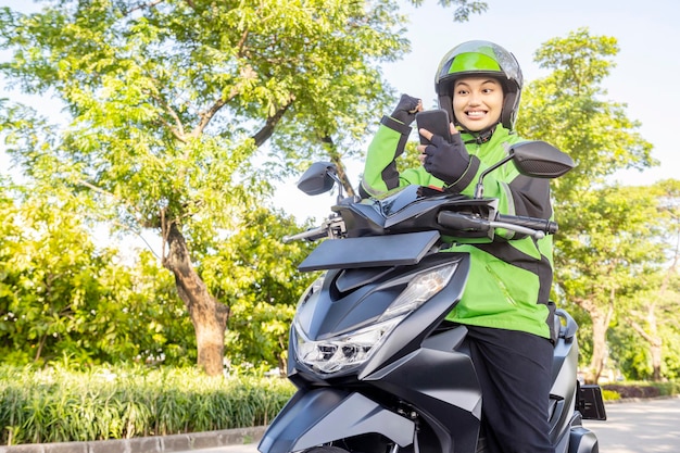 Asian woman works as a motorcycle taxi driver checking order on her mobile phone