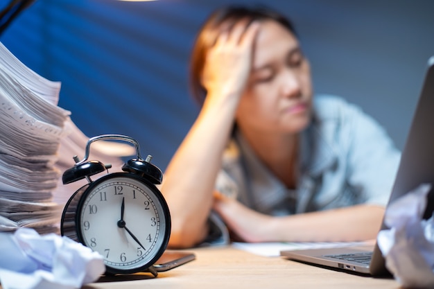 Asian woman writing documents in overtime at night.Working deadline in office.Officer girl headache and busy with her job.Unhappy and stress.