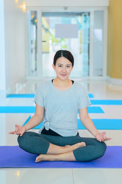 Asian woman yoga breathing and meditation alone in fitness gym. Indoor exercise and workout for healthy and wellness.