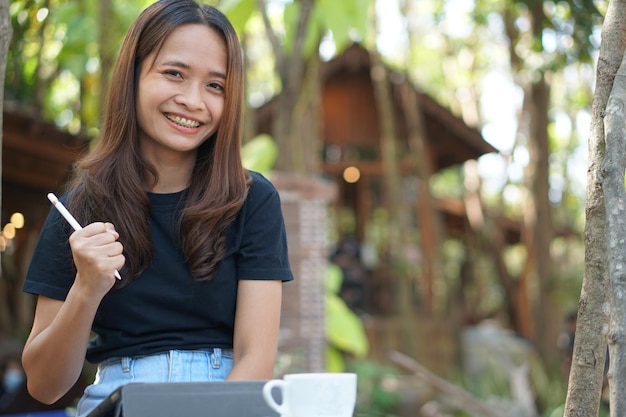 Asian women are happy to sit and work in a coffee shop There are green trees surrounded by nature Business planning is a good idea