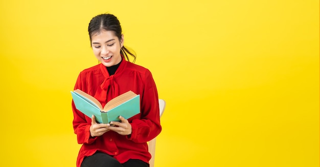 Asian women are reading a book or novel, enjoying and happy, the woman is opening a book in the hand and accidentally read it on yellow background with copy space.