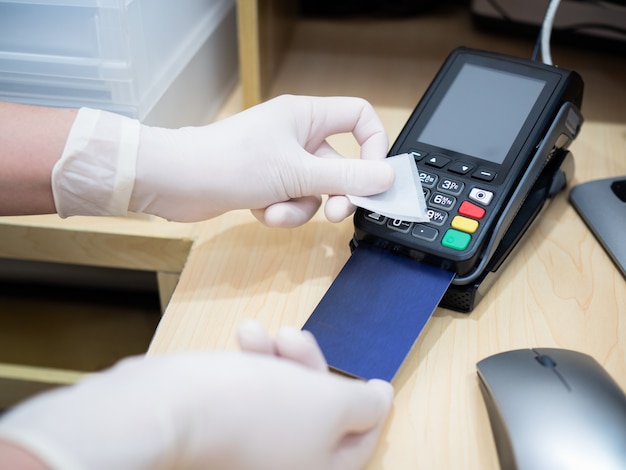 Asian women at cashier counter use alcohol pad to clean credit card terminals or machine before swiping client card, prevent spreading of coronavirus. Covid-19, coronavirus, social distance concept.