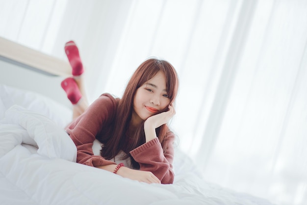 Asian women happily lie on the white bed in the house.