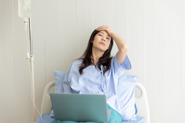 Asian women patient lying in a hospital bed using a laptop