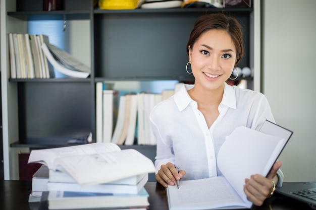 Asian women student smiling and reading a book for final exam at home