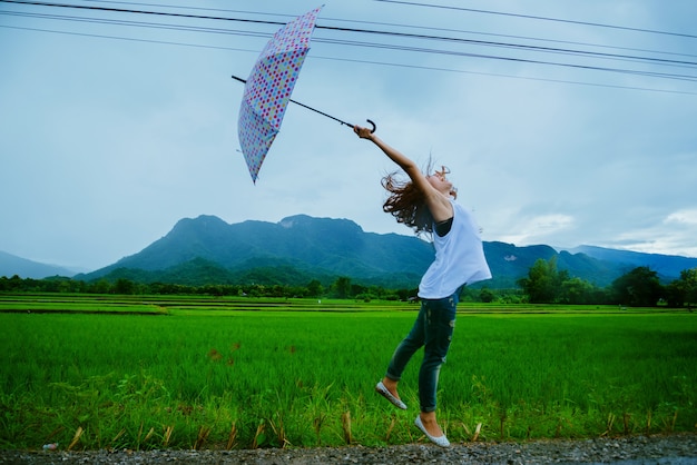 Asian women travel relax in the holiday. The women stood holds an umbrella in the rain happy and enjoying the rain that is falling. travelling in countrysde, Green rice fields, Travel Thailand.