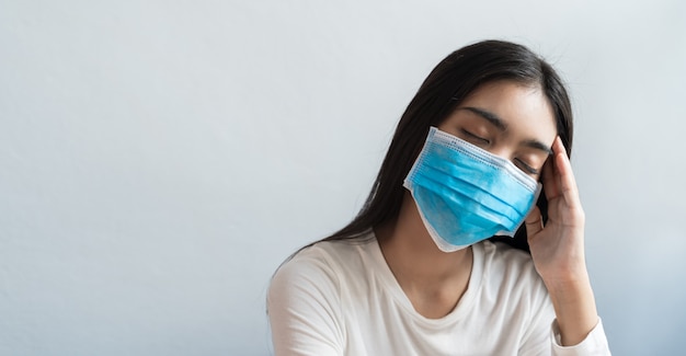 Asian women wear a mask are holding their heads because of headaches. She has a fever and migraine because of stress or sleep late, low sleep, insufficient rest in healthy concept with copy space.