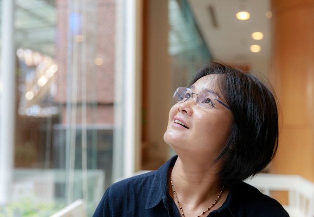 Asian women with short hair, short sleeve dress blue glasses sitting by the window glass.