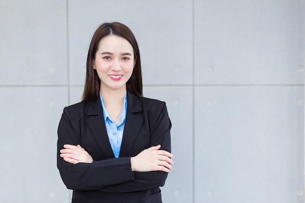 Asian working female who has long hair wears black formal suit with blue shirt  she arm crossing