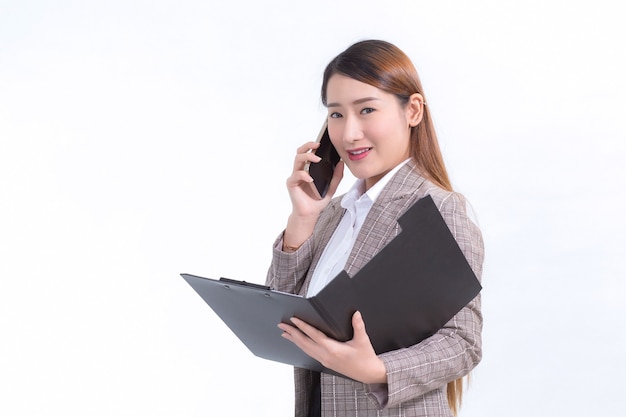 Asian working woman in formal suit with white shirt is calling telephone and opens document file or clipboard to check data.