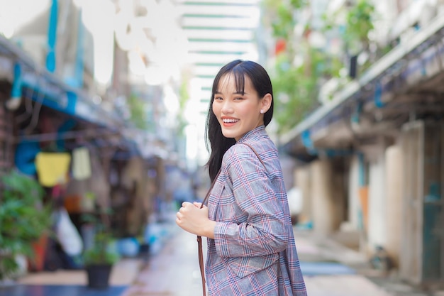 Asian working woman who wears a Brown striped blazer and shoulder bag smiles happily.