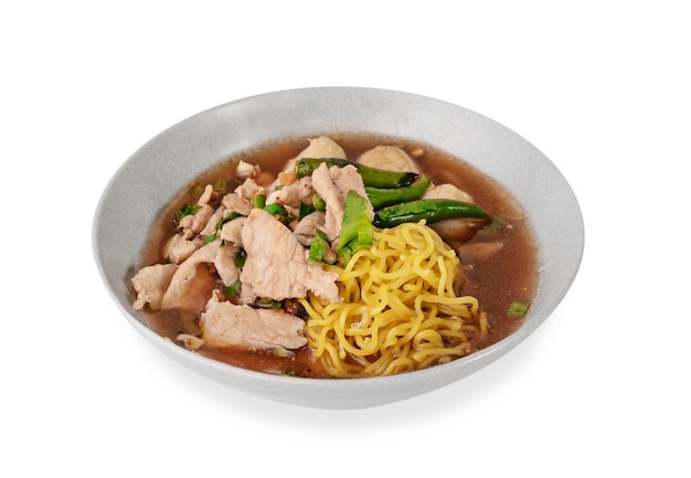 Asian yellow noodles with pork and vegetables in bowl over white background