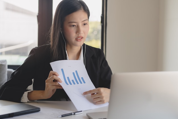 Asian young business woman holding paperwork and video calling via laptop