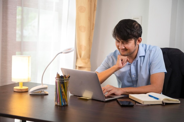 Asian young businessman smiling typing on laptop Happy businessman working on strategy at home office desk home office plan