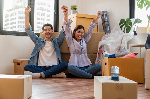 Asian young couple are glad after successfull packing the big cardboard box for moving in 