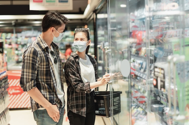 Asian young couple in protection mask stand to choose for shopping frozen food amid coronavirus outbreak