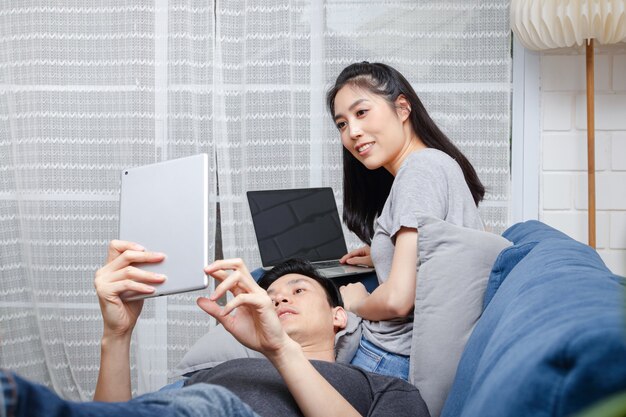 Asian young couple Sit and relax on their blue sofa in their home during the holidays. Family concept, work at home.