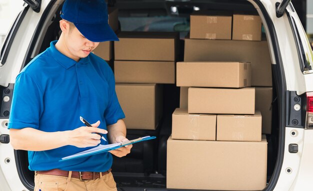 Asian young delivery man courier in uniform hold documents clipboard checking list parcel post boxes near a car for service shipment to customer, Online shopping service concepts