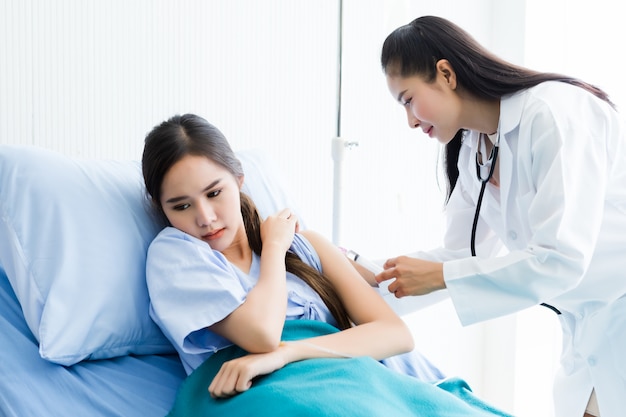 Asian young female doctor with syringe to the arm of Asian young female patient on Bed for better healing In the room hospital 