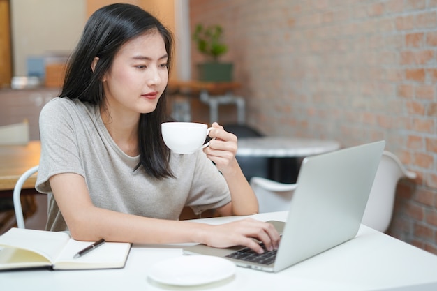 Asian young freelancer using laptop and working while drink coffee at home office.