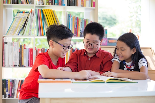 Asian young girl & boys reading books on desk and happiness feel at library in thier school