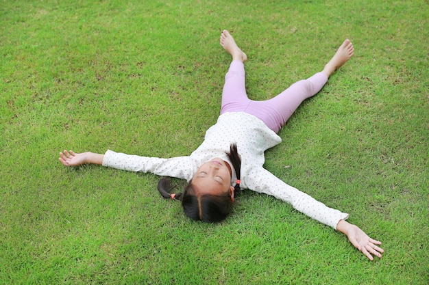 Asian young girl child lying on green lawn at the garden Kid lies on grass