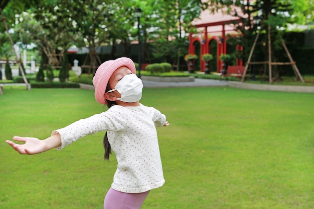 Asian young girl child wearing medical mask with open wide arms due covid19 on the garden