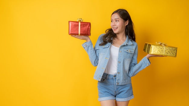 Asian young girl in jeans holding two gifts and thinking to chose