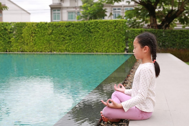 Asian young girl kid practicing mindfulness meditation sitting near the pool