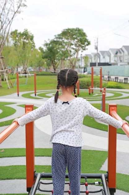 Asian young girl playing on equipment at a playground Rear view